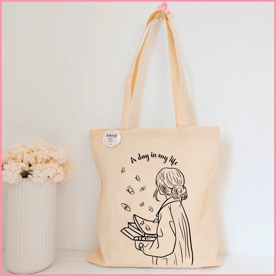 Tote bag color beige con diseño de una mujer con libros y mariposas y la frase A day in my life