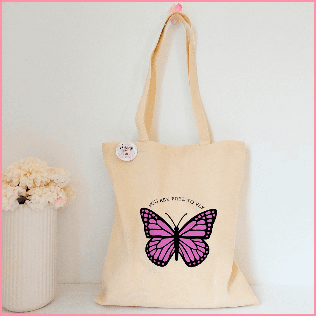 Tote bag color beige con diseño de mariposa morada y la frase YOU ARE HERE TO FLY