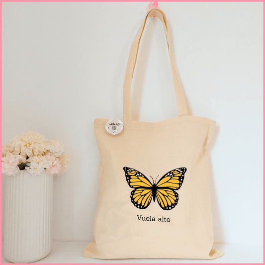 Tote bag color beige con diseño de mariposa naranja y la frase Vuela alto