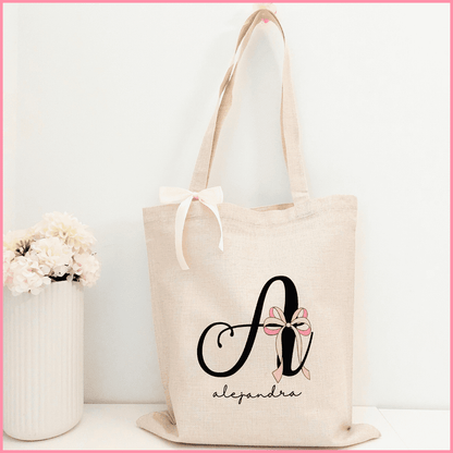 Tote bag  color beige personalizada con el nombre e inicial a elegir adornado con el diseño Coquette que incorpora un lazo rosa