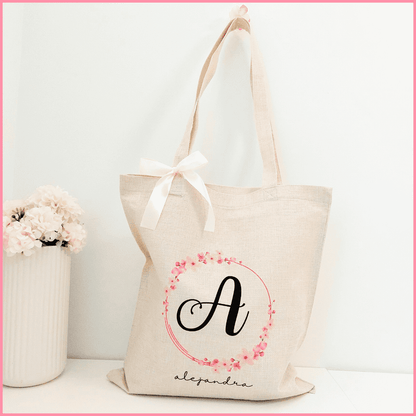 Tote bag  color beige personalizada con el nombre e inicial a elegir adornado con un diseño elegante de flores rosas en forma de corona rodeando la inicial